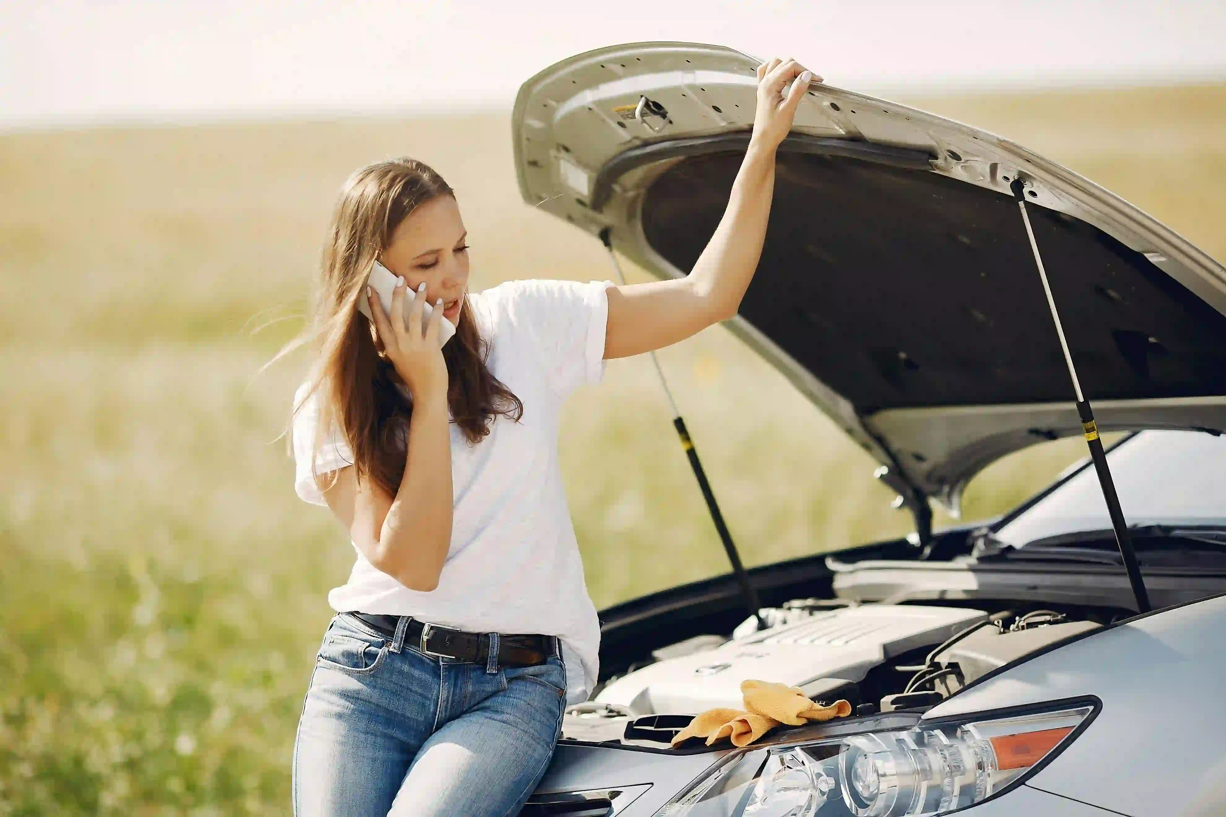 Mujer hablando por teléfono mientras revisa el motór de su coche.